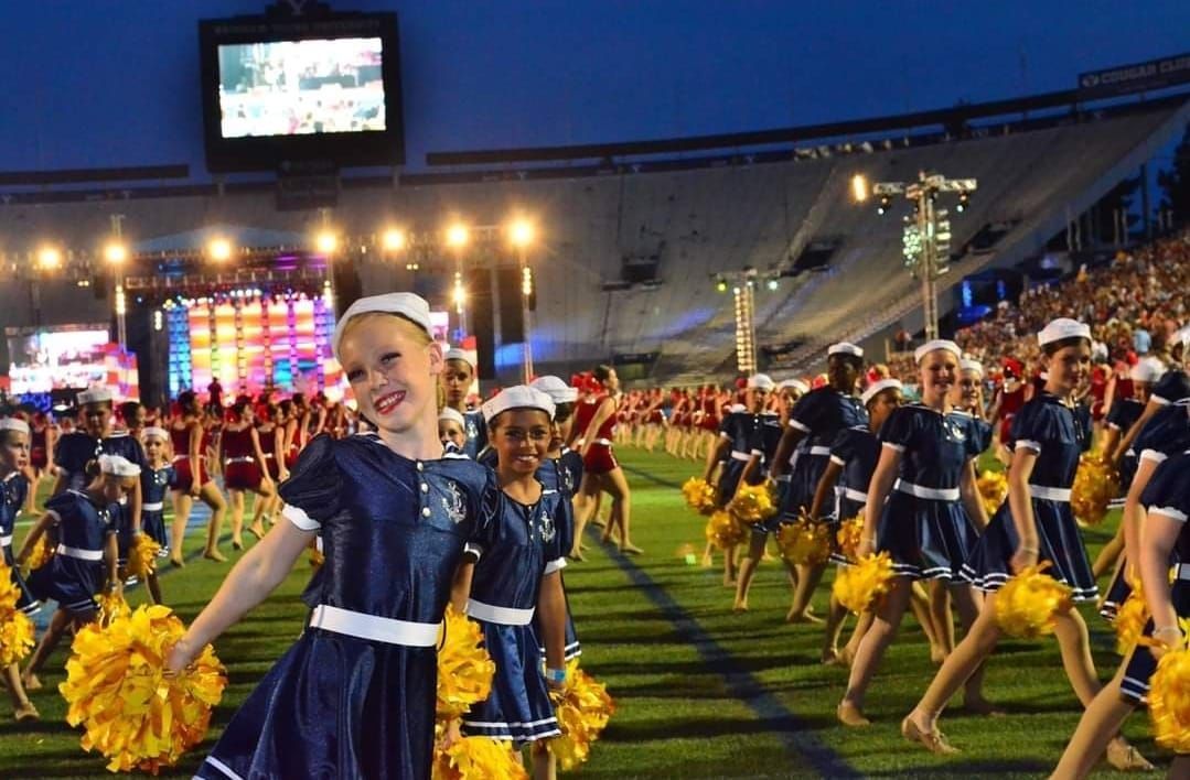 A group of cheerleaders are walking on a field with yellow pom poms.