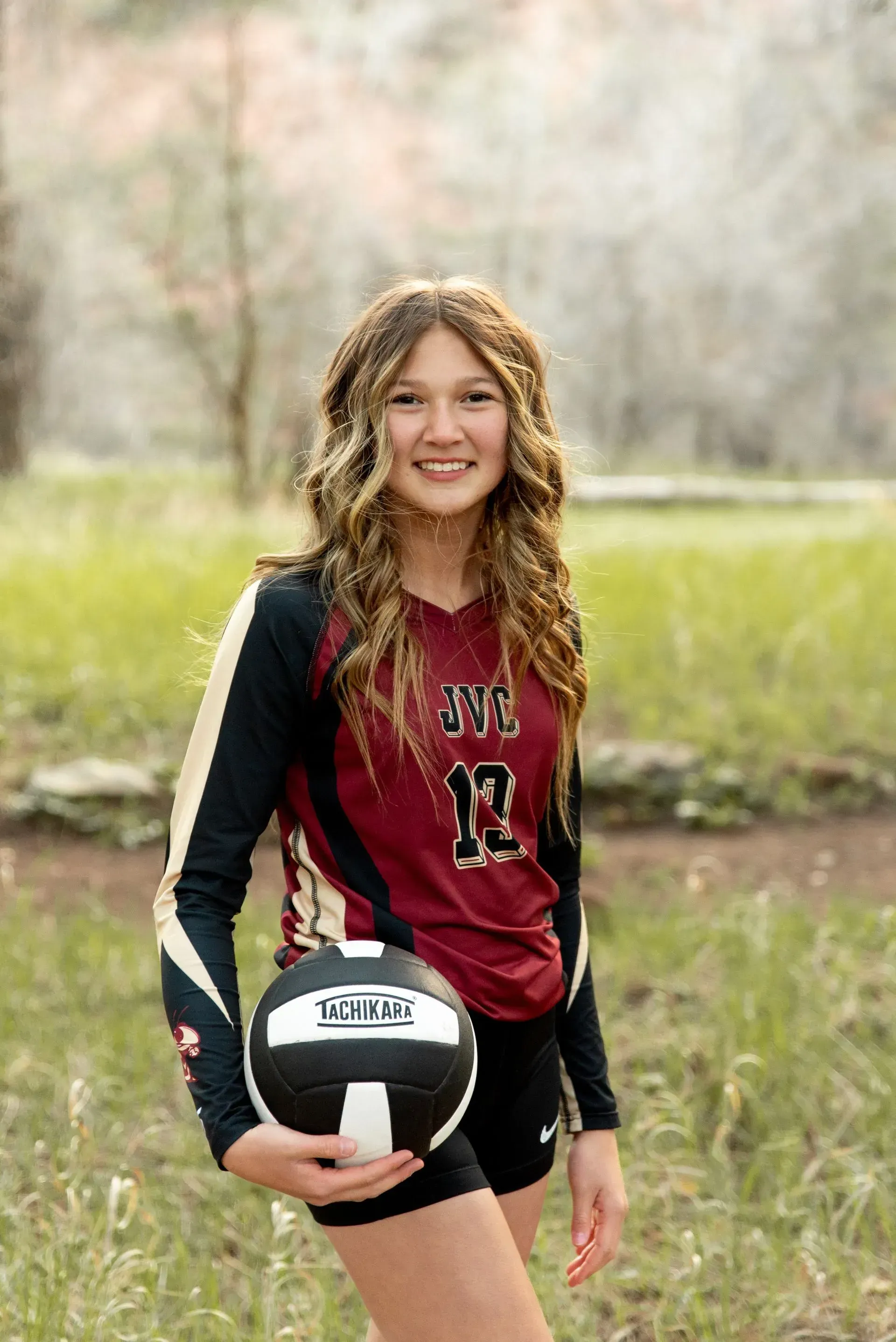 A young woman is holding a volleyball in a field.