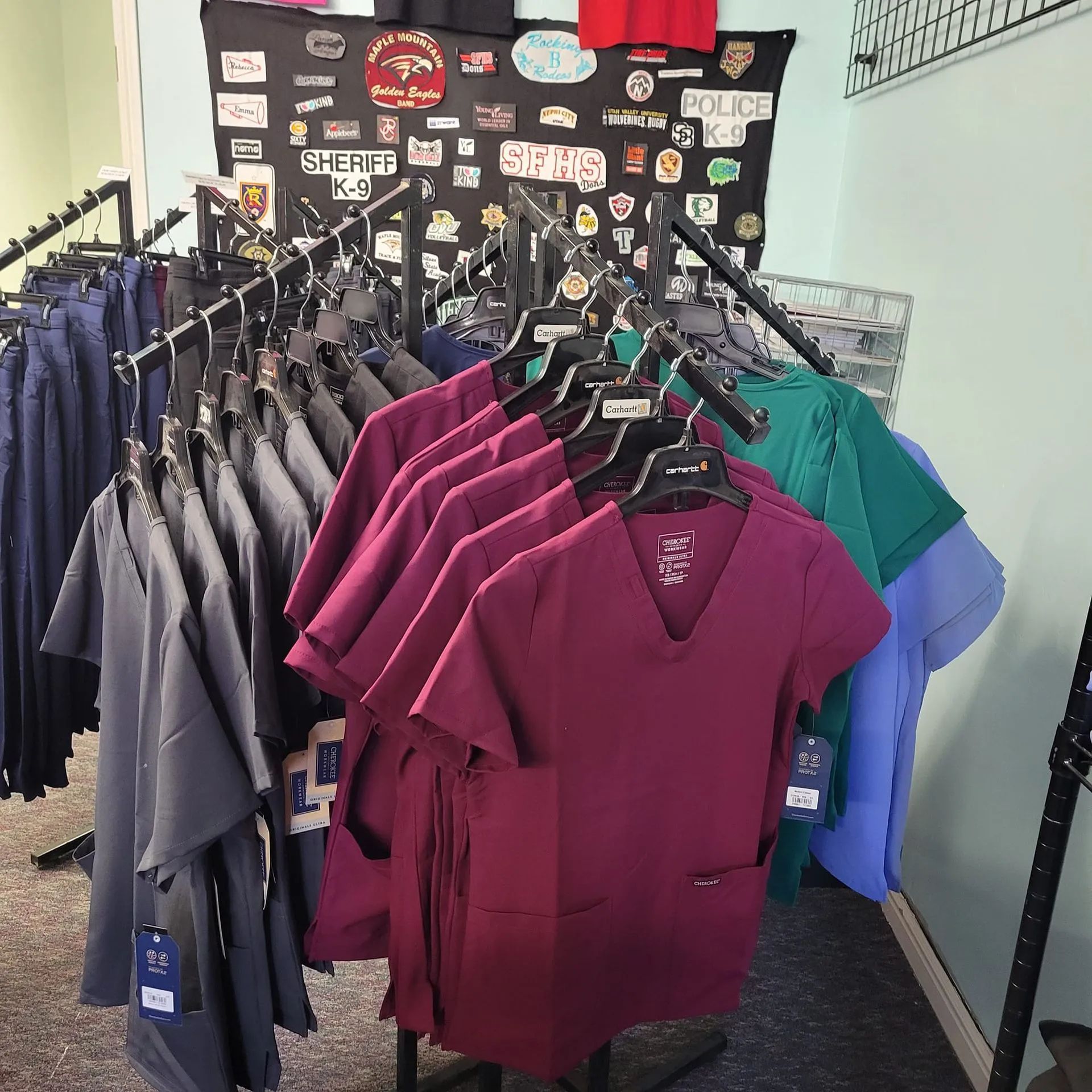 Clothes rack with various colored scrubs: blue, grey, burgundy, and green.