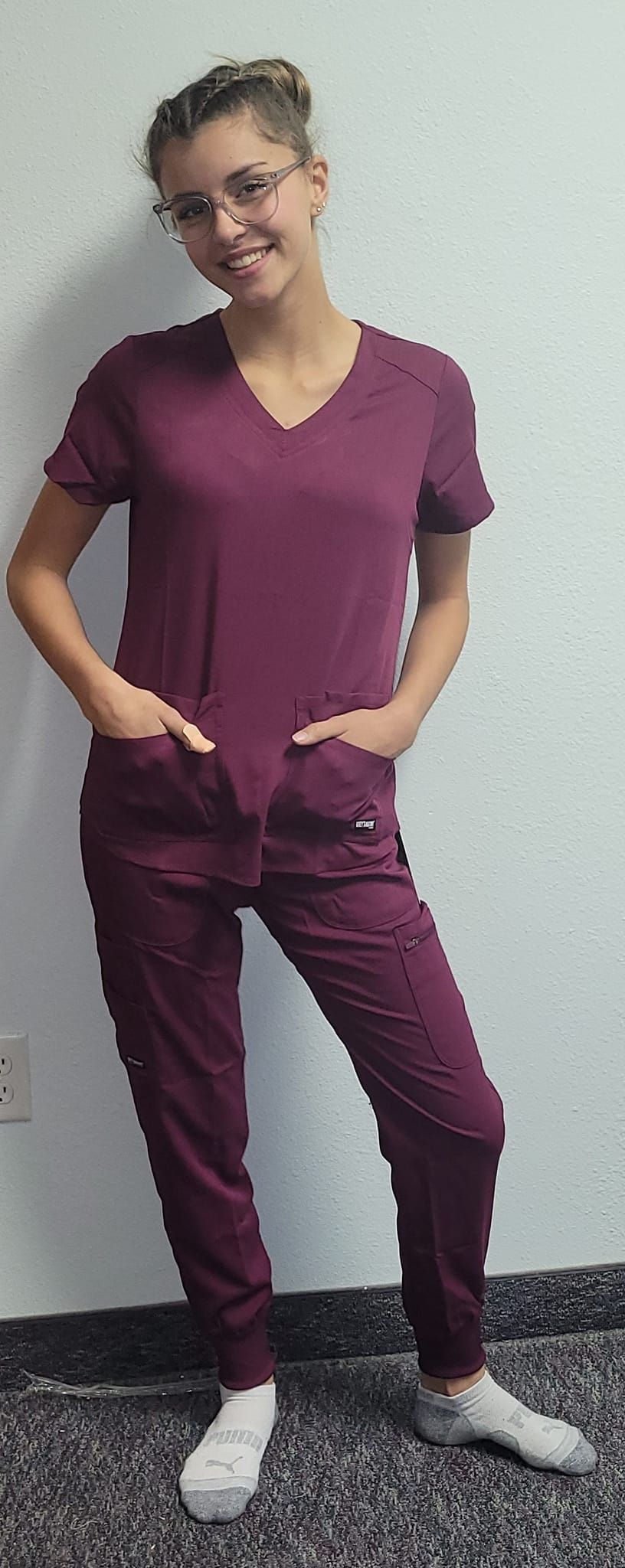 A woman in a purple scrub suit is standing with her hands in her pockets.
