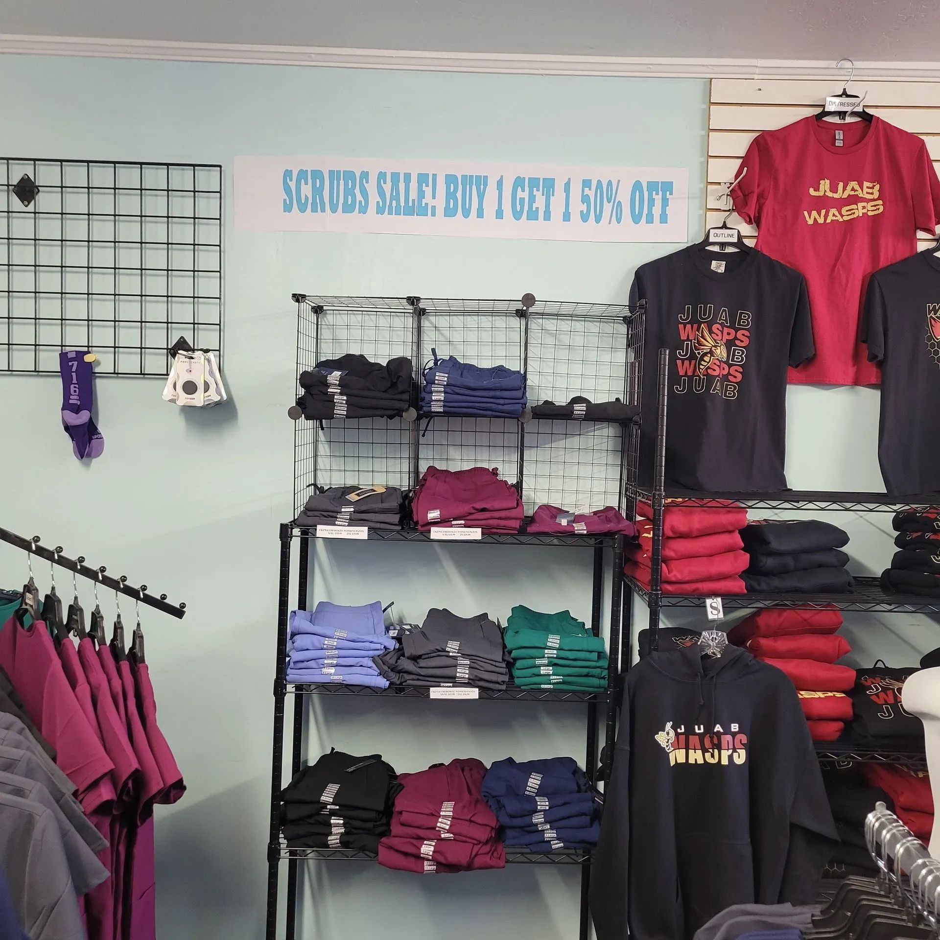 Clothing store interior with scrubs and t-shirts on display; a sale sign is visible.