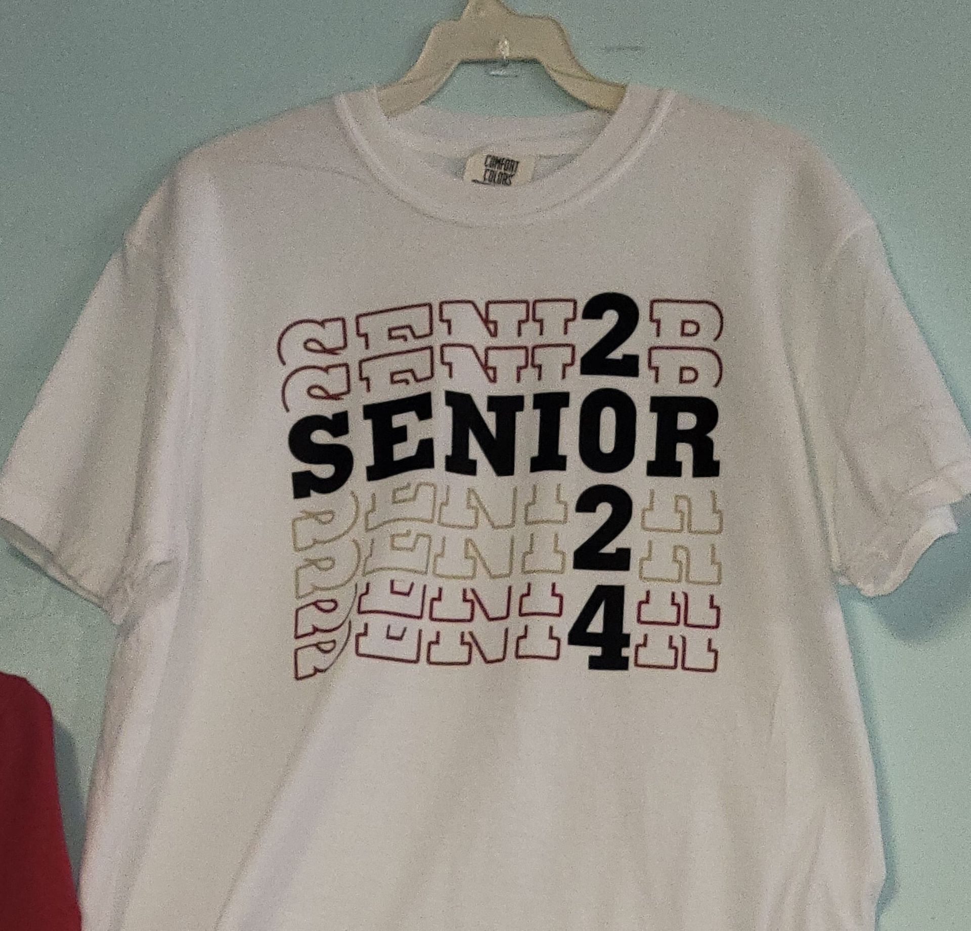 A white t-shirt that says senior 2 is hanging on a hanger