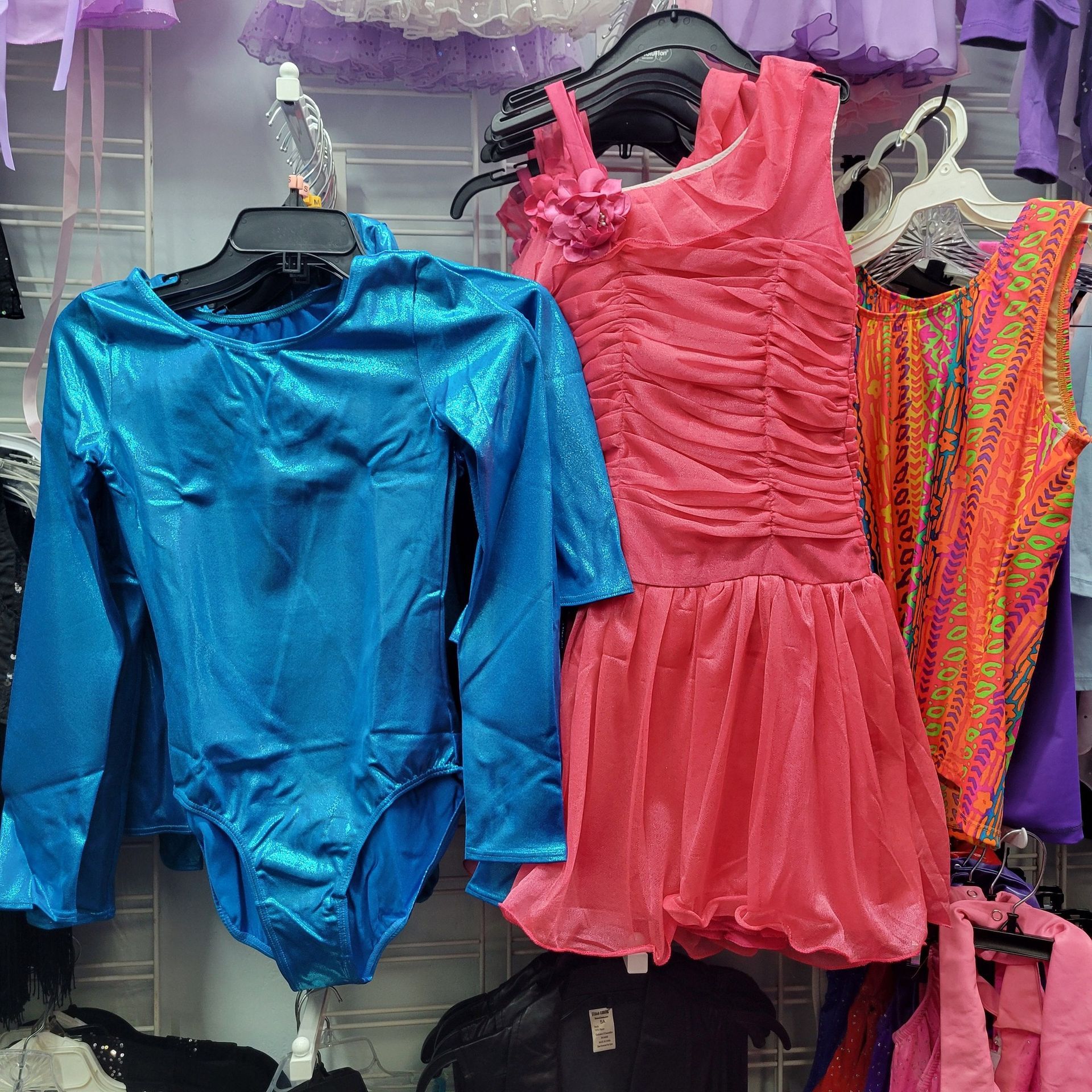 A blue leotard and a pink dress are hanging on a rack