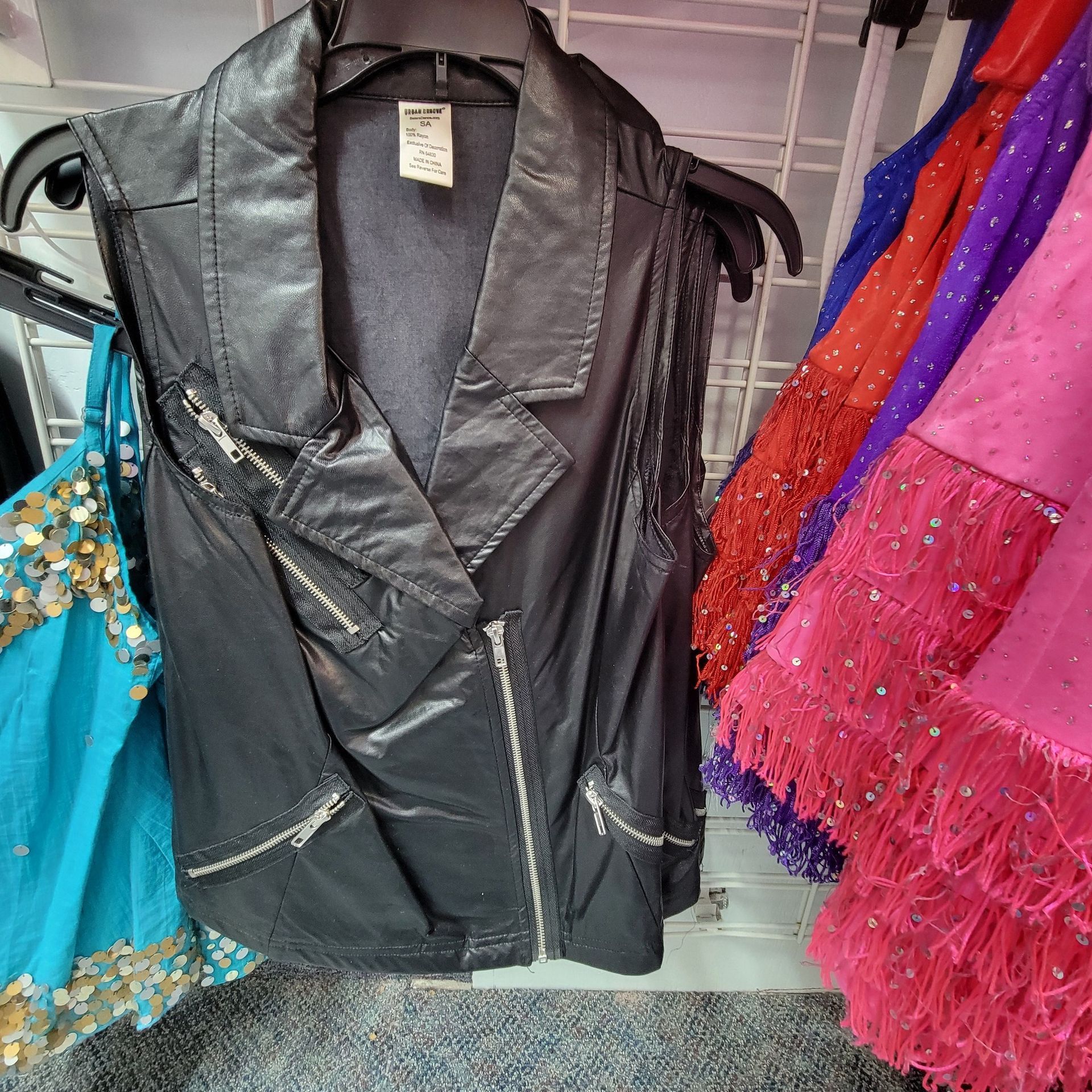 A black leather vest with fringe is hanging on a rack