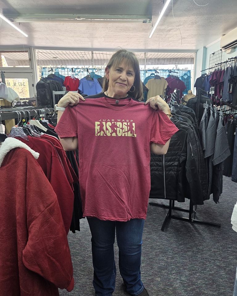 A woman is holding a red baseball t-shirt in a clothing store.