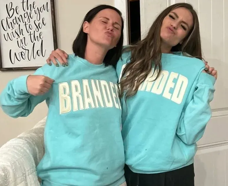 Two women wearing light blue sweatshirts with the word brand on them