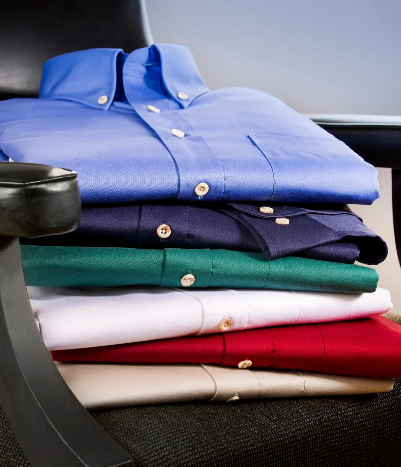 A stack of shirts of different colors sits on a chair