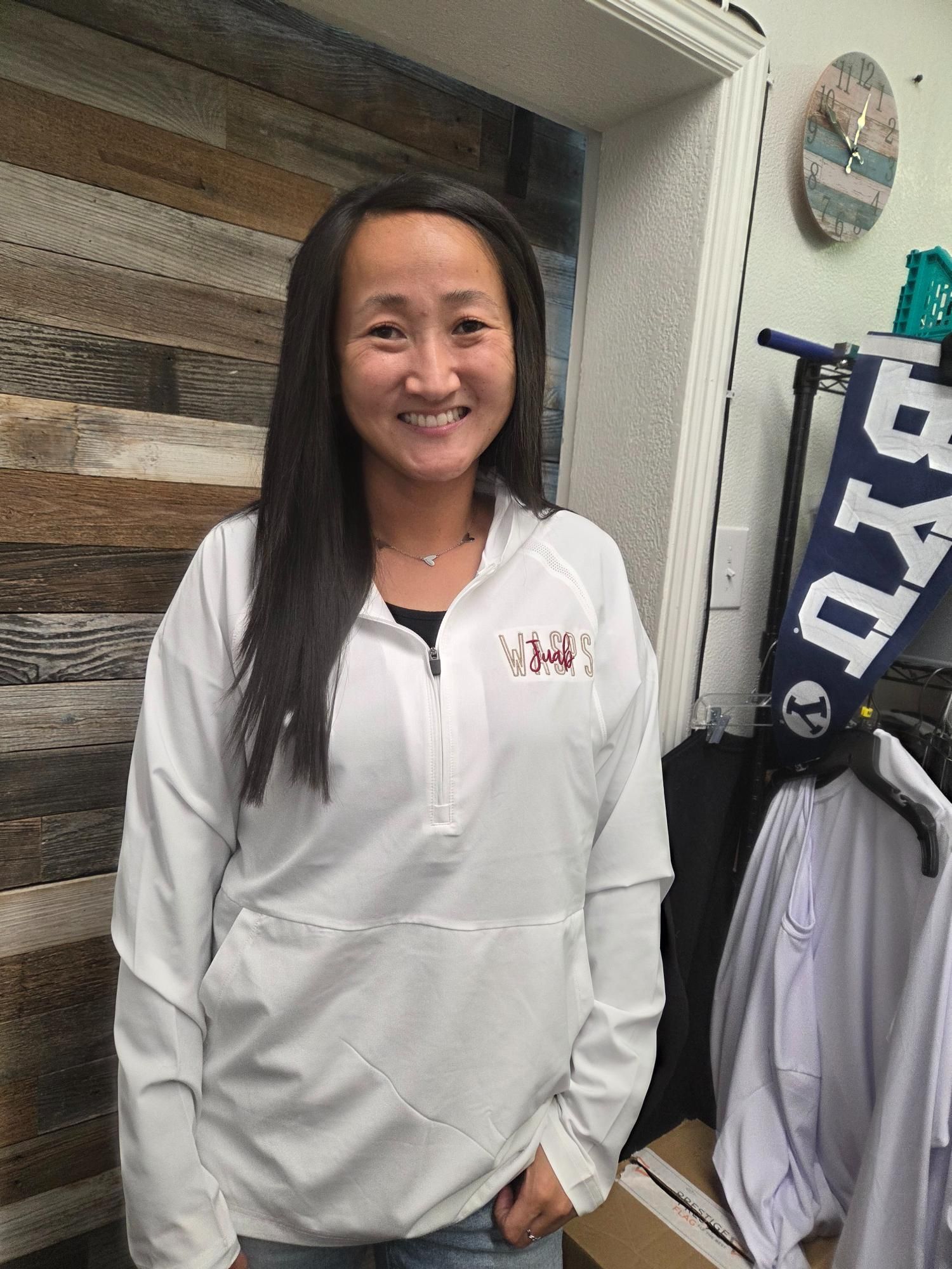 Woman in white jacket smiling in a shop, BYU banner visible.