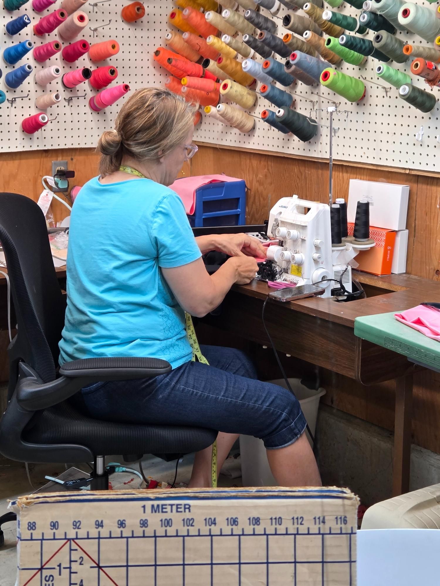 Woman using a serger at a sewing table, surrounded by thread spools.