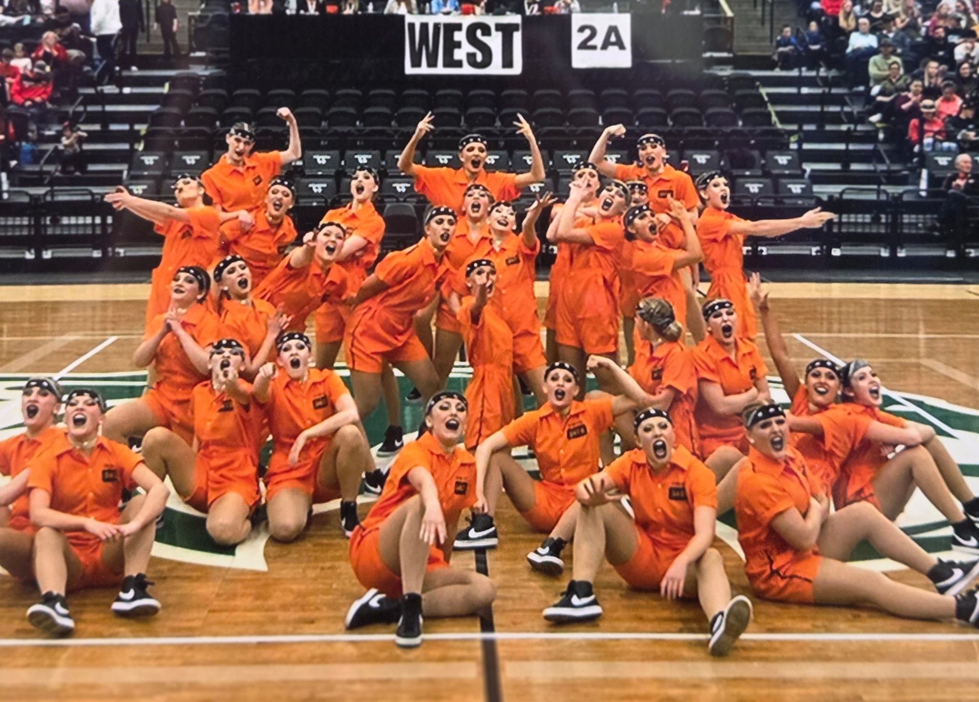 Group of dancers in orange jumpsuits striking poses on a basketball court. 