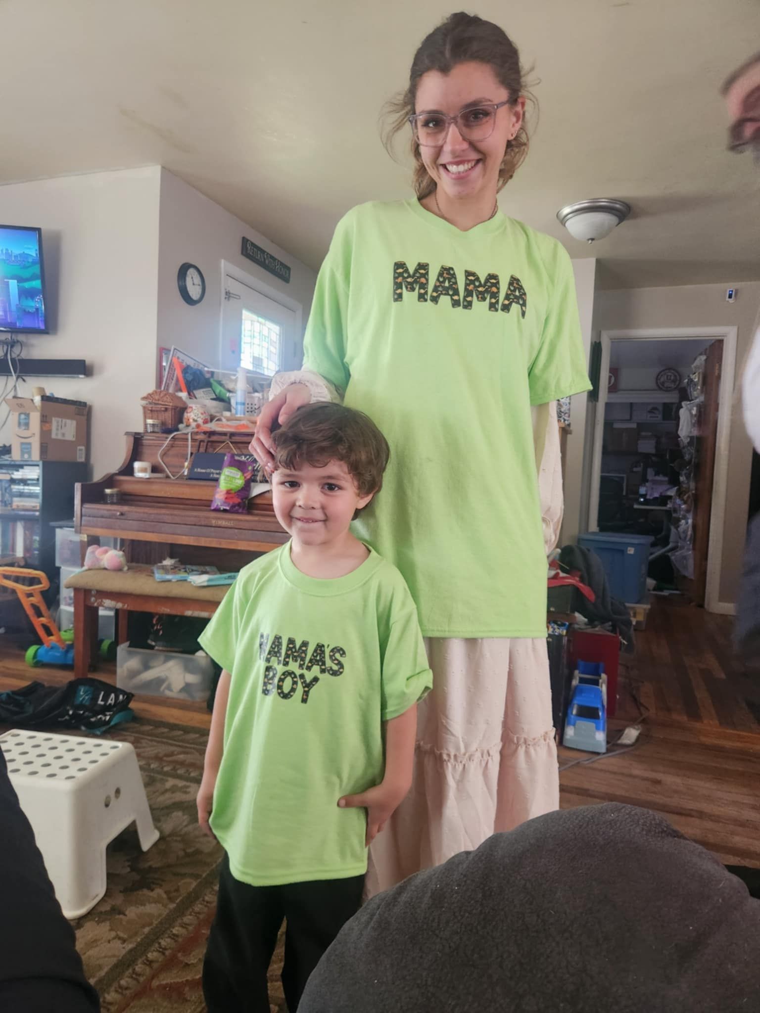 Woman and child smiling, wearing matching green shirts that say 