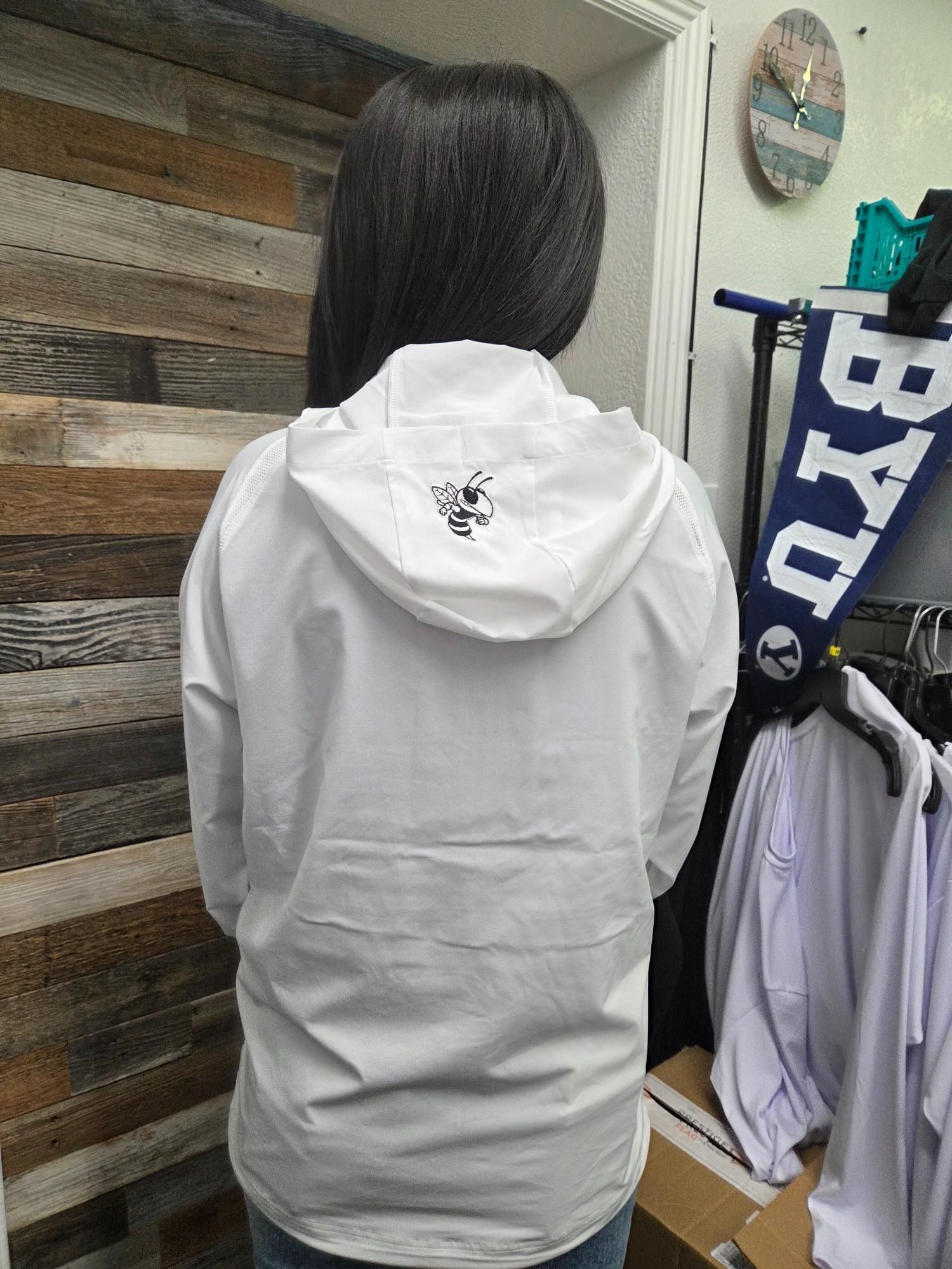 Person wearing a white hooded jacket. Back view. In a store with a BYU pennant and shirts.