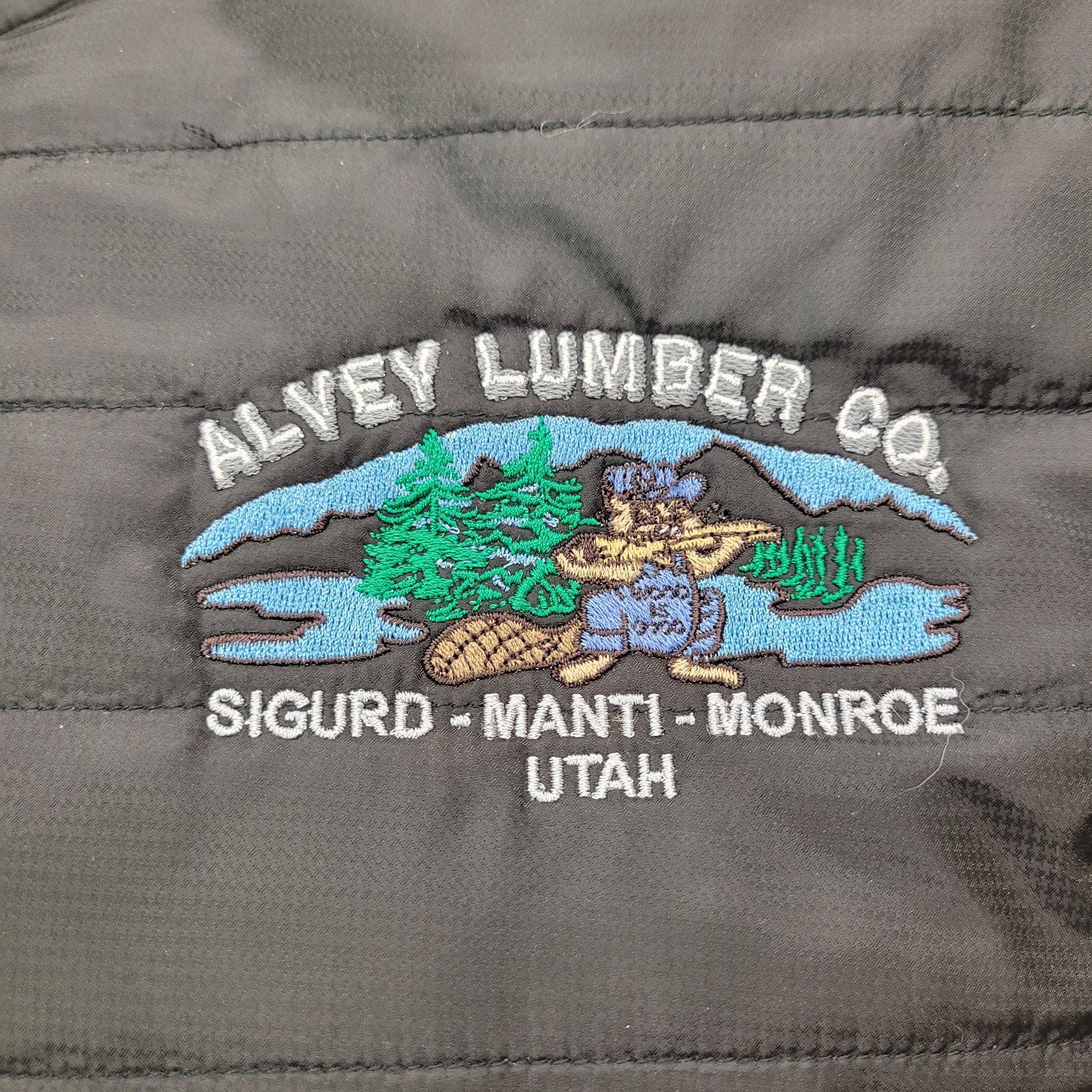 Embroidered Alvey Lumber Co. logo on black jacket. A beaver holding a saw in front of trees.
