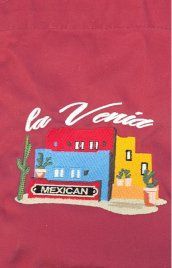 Embroidered sign for La Venia Mexican restaurant featuring colorful buildings and a cactus.