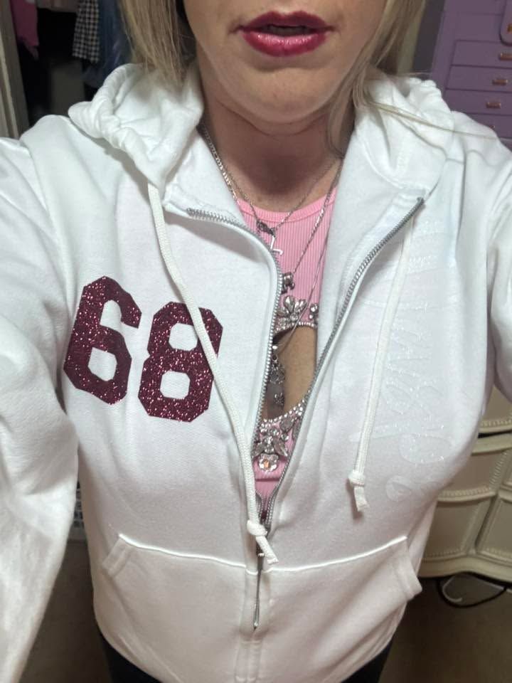 Woman in white zipped hoodie over pink shirt, wearing necklace; 