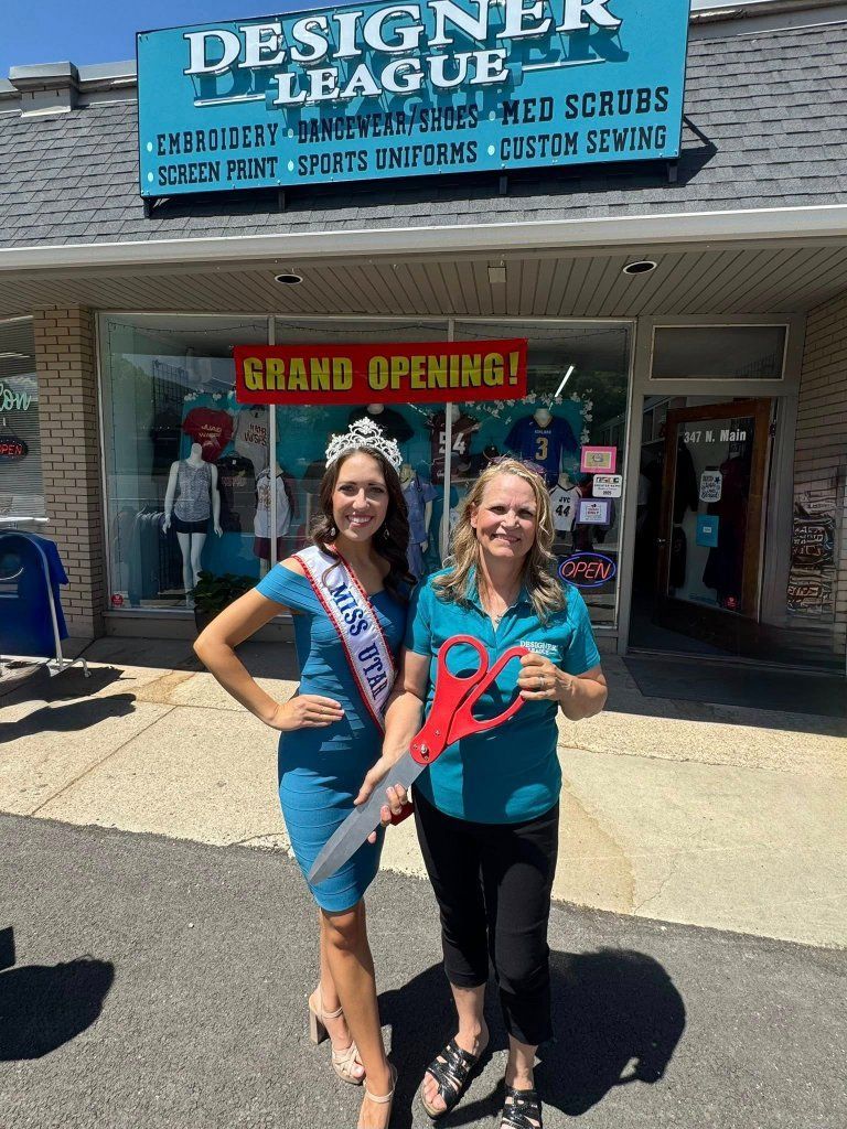 Two women holding giant scissors at a Grand Opening in front of 