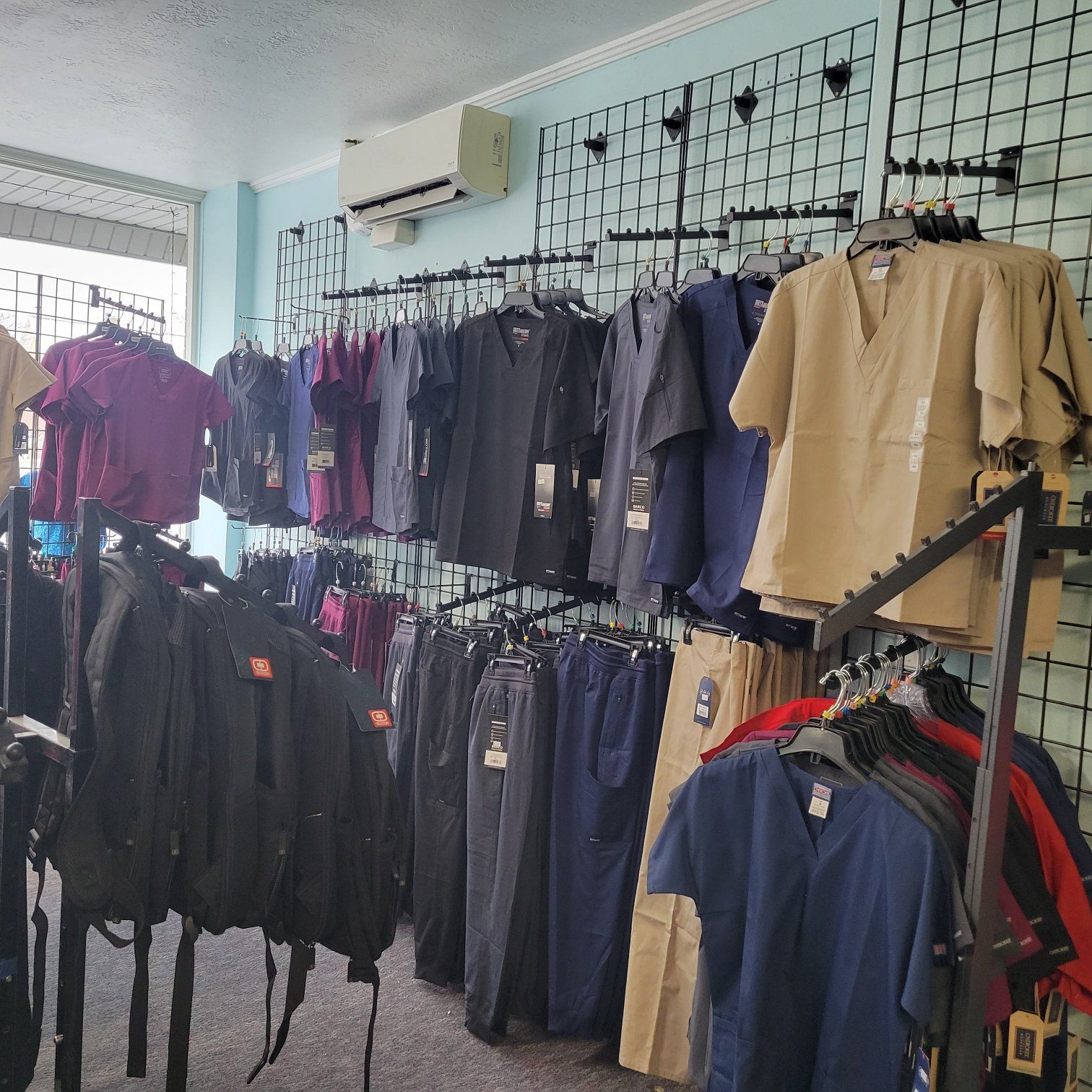 Inside a medical scrubs store, colorful scrubs hang on black wall racks.
