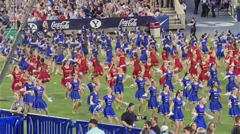 Dancers in blue and red uniforms perform on a football field, BYU stadium, in front of cheering crowd.