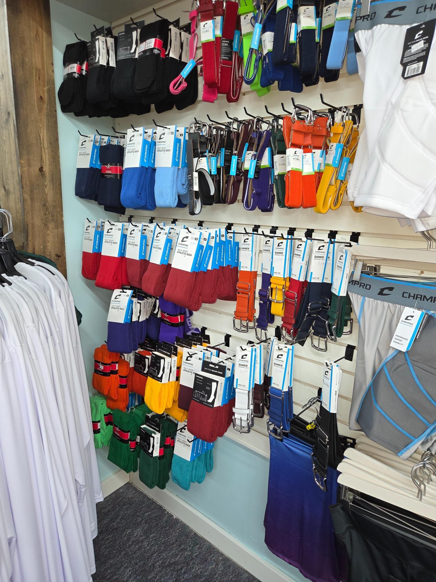 A retail display of colorful socks hanging on a wall; other clothing visible on racks nearby.