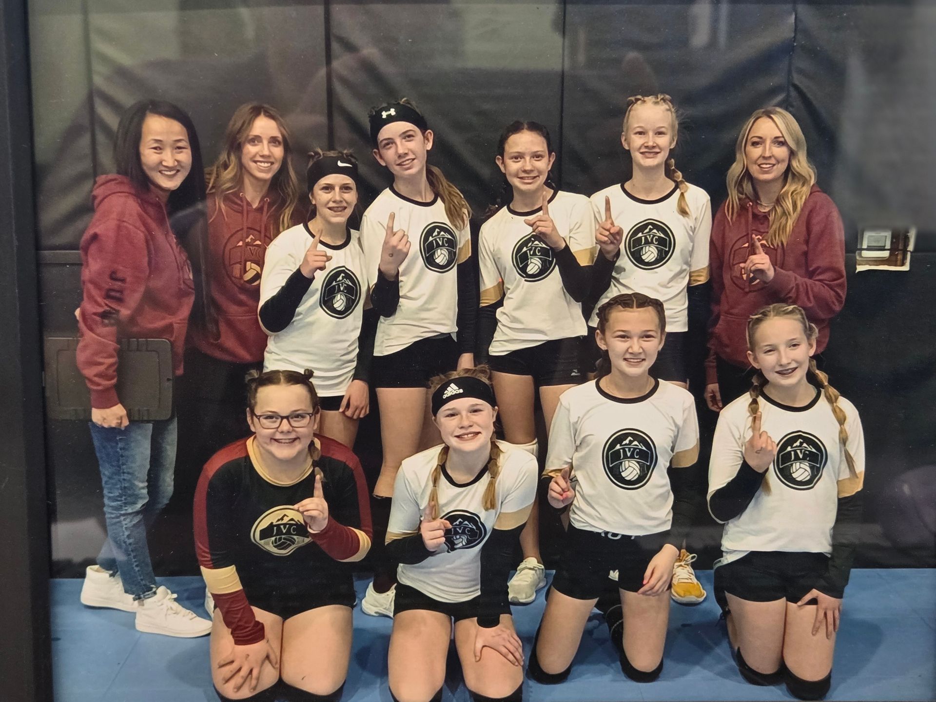 Volleyball team in white/black jerseys with gold accents and coaches, holding up 