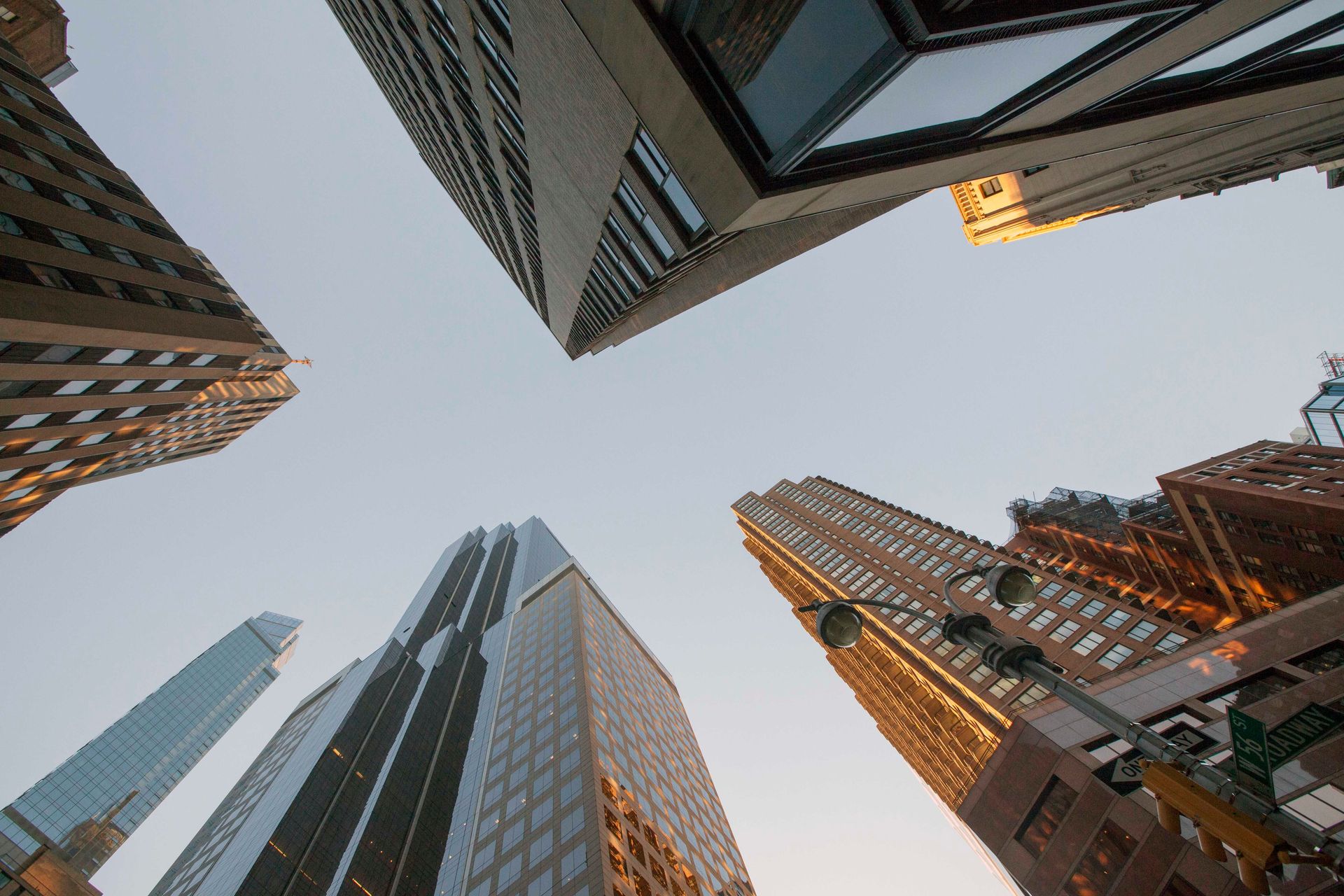Skyscrapers viewed from below against a clear sky, with warm sunset reflections on glass towers