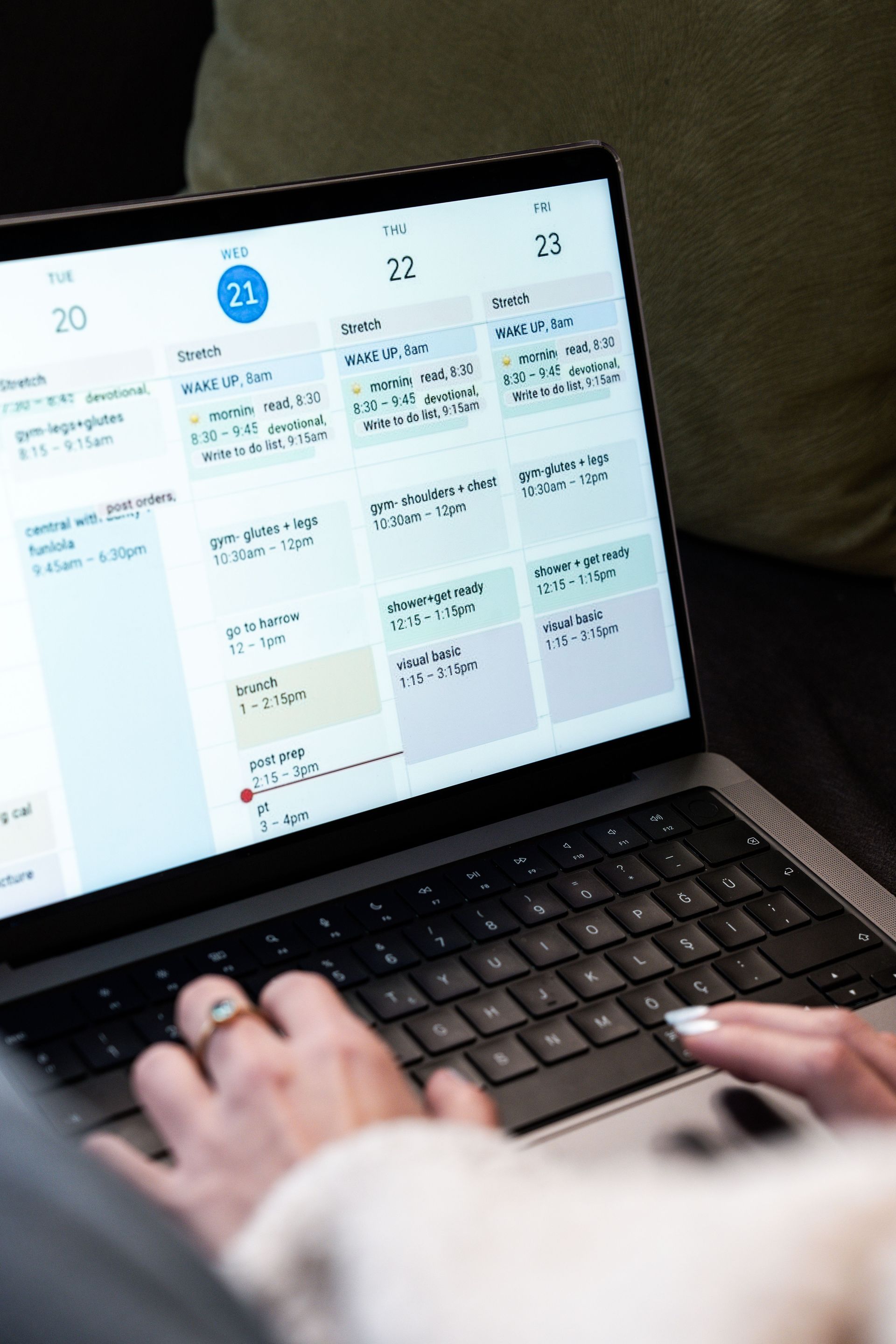 Hands typing on a laptop displaying a calendar schedule in a dim room.