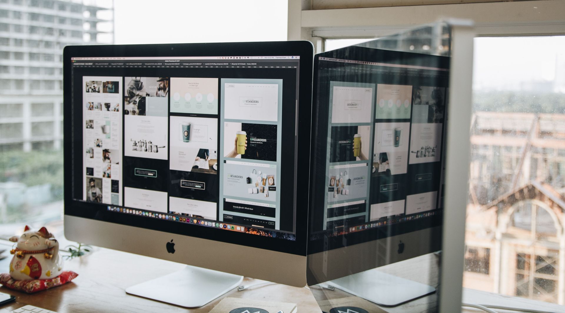 Dual-monitor desktop displaying a design layout in a bright office by a window