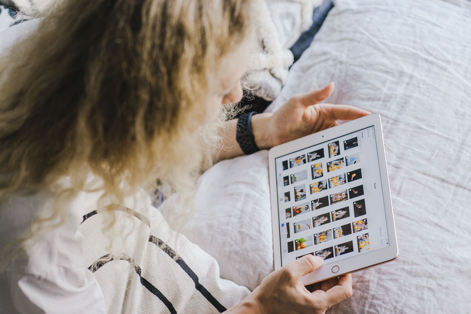 Woman holding a tablet showing a photo gallery while reclining on a bed