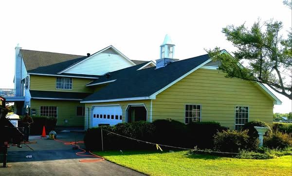 A large yellow house with a black roof and a garage