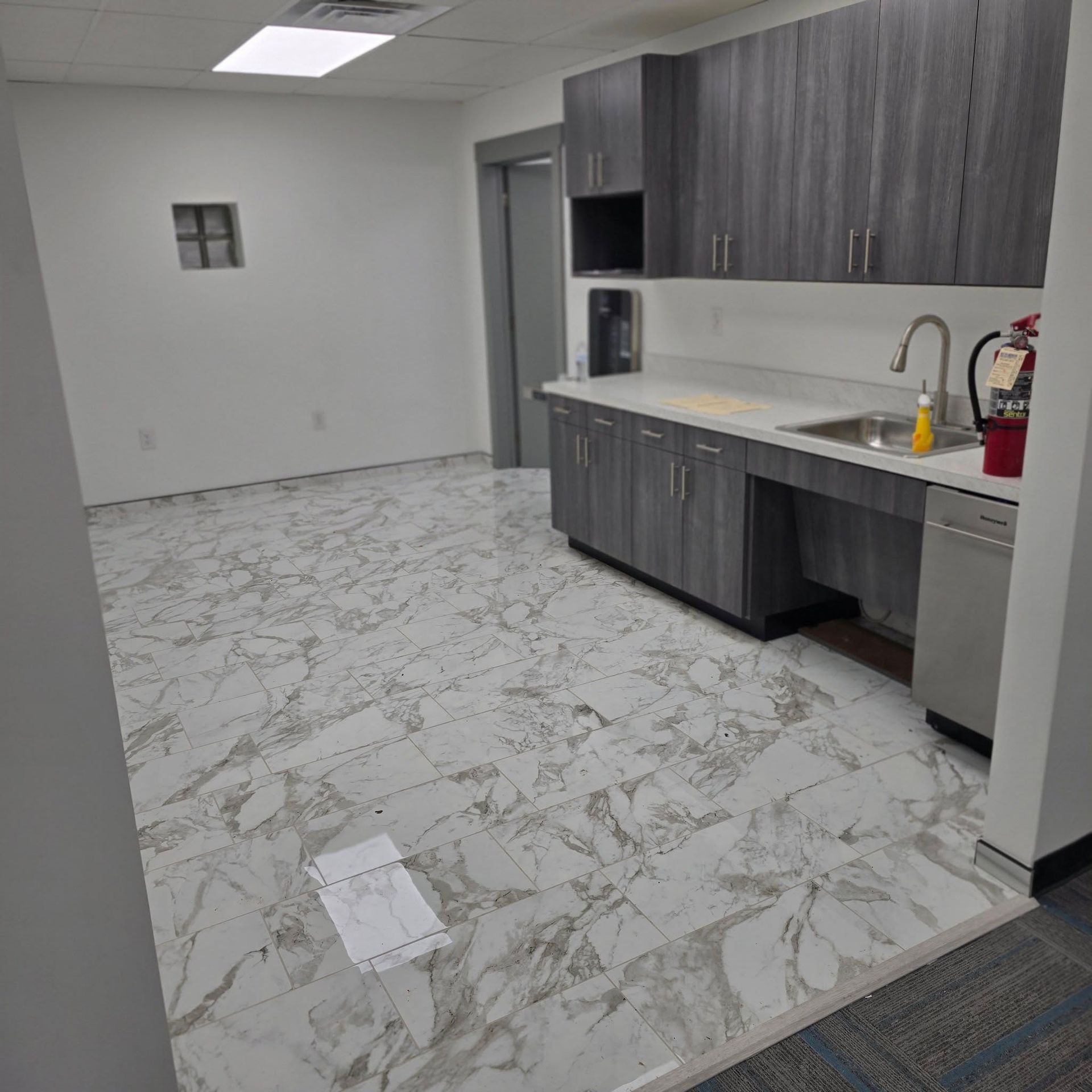 A kitchen with marble floors , gray cabinets , a sink , and a fire extinguisher.