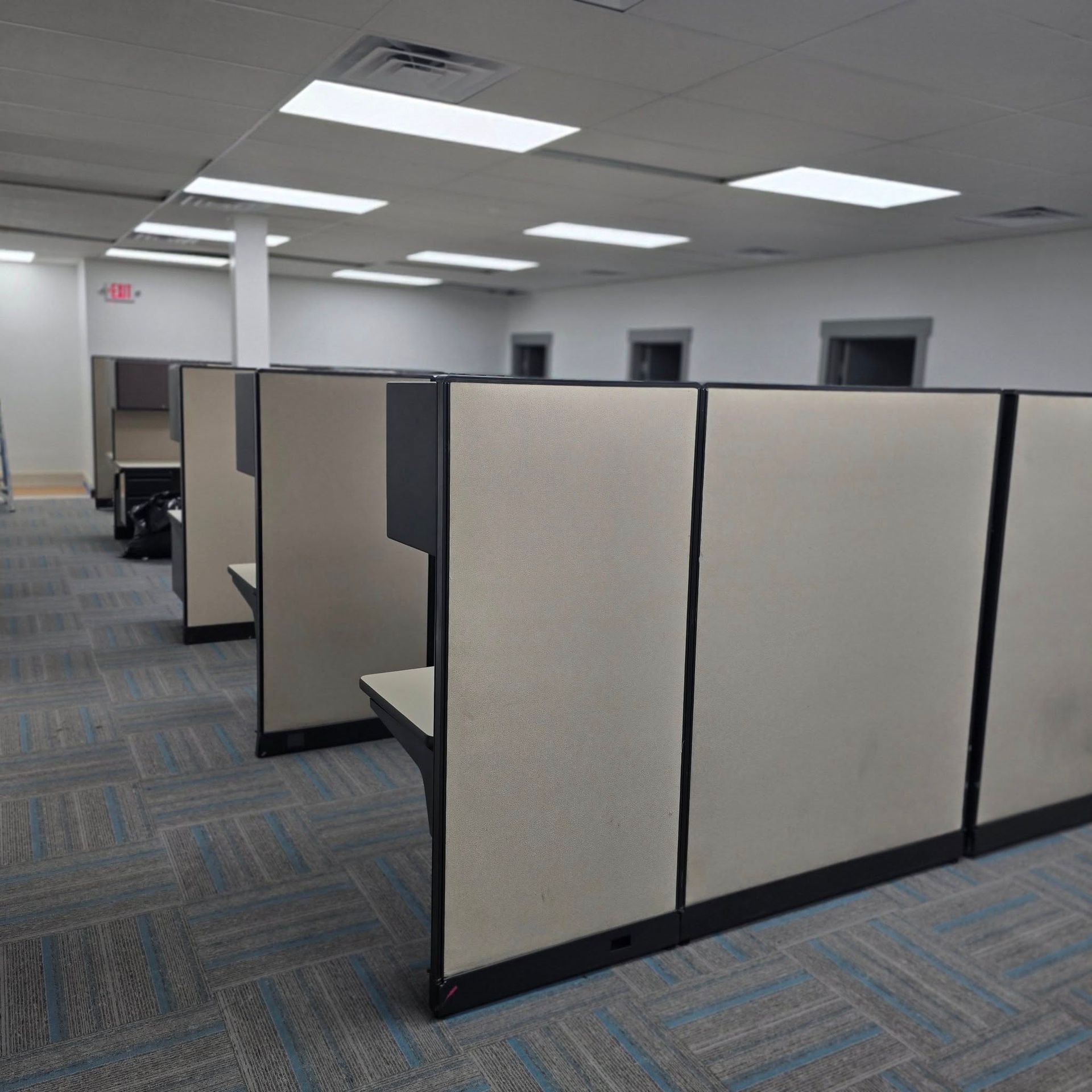 A row of cubicles in an office with an exit sign in the background