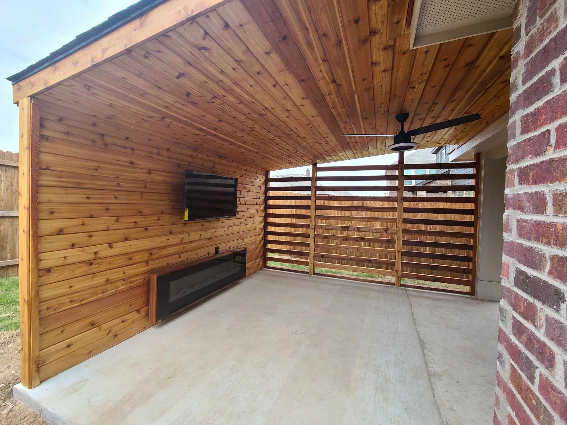 A wooden patio with a television mounted on the wall and a ceiling fan.
