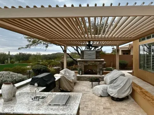 A patio with a pergola , a fireplace , chairs , a table and a grill.