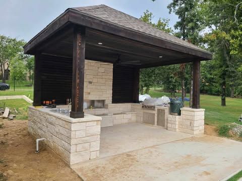 A gazebo with a brick wall and a wooden roof is being built in a backyard.
