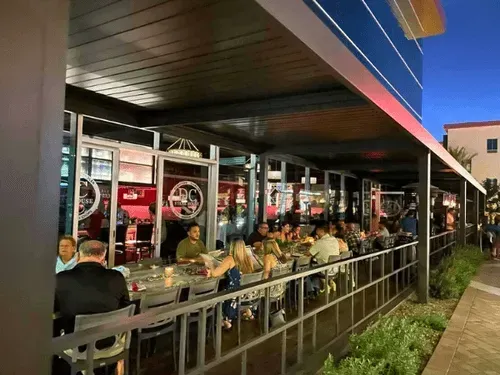 A group of people are sitting at tables outside of a restaurant.