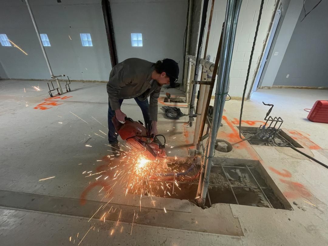 A man is cutting a hole in the floor with a grinder