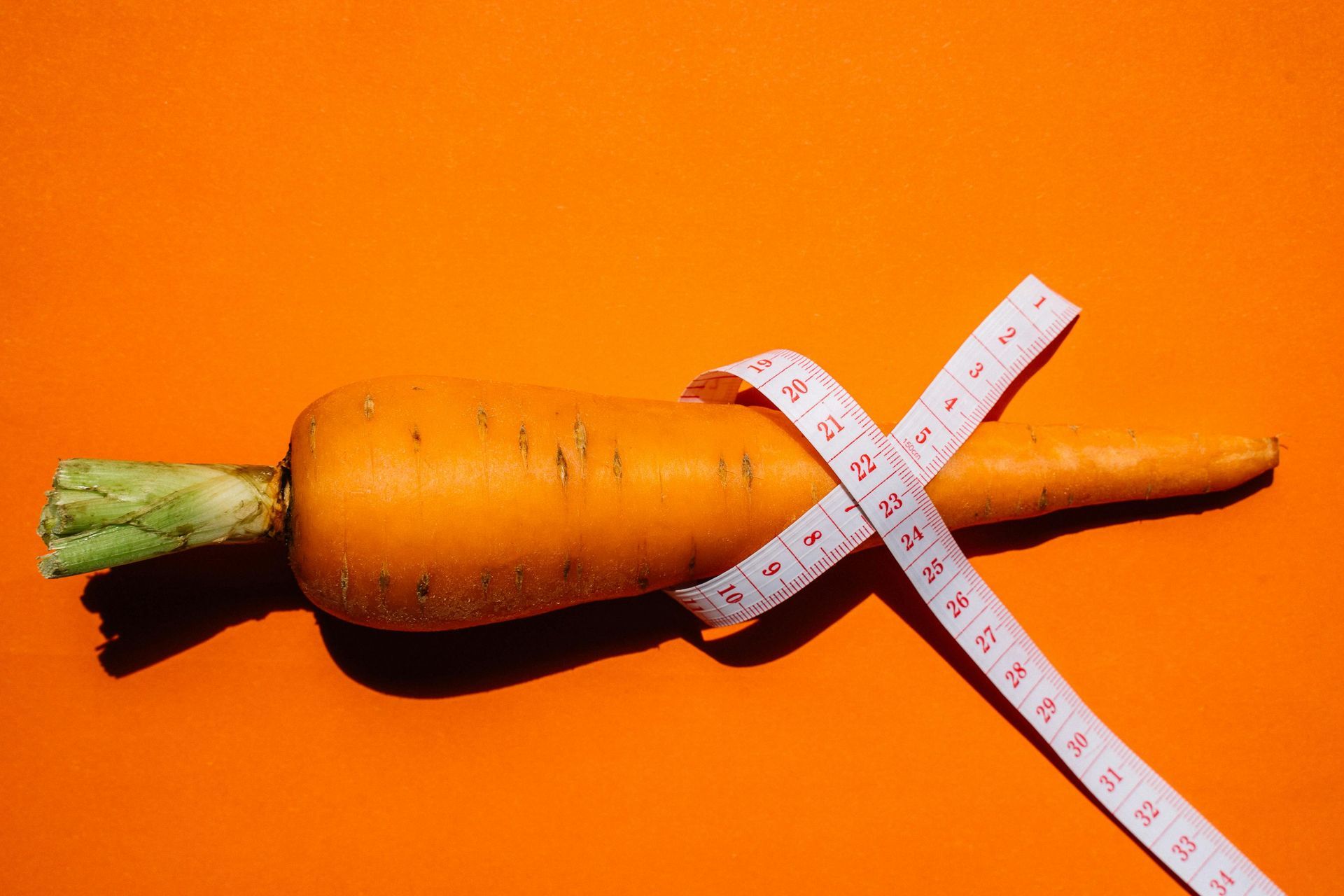 Carrot wrapped with a white measuring tape on an orange background.