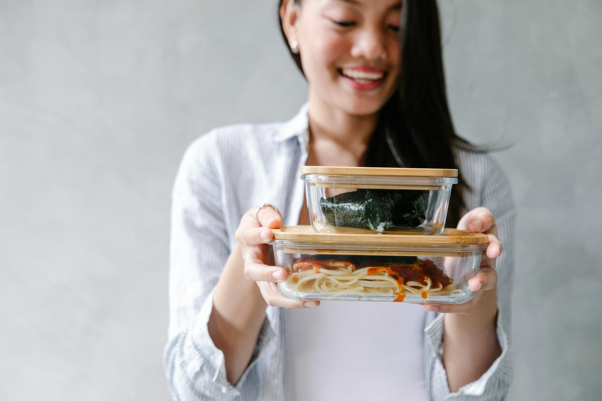 Smiling person holds two glass food containers with food and bamboo lids.
