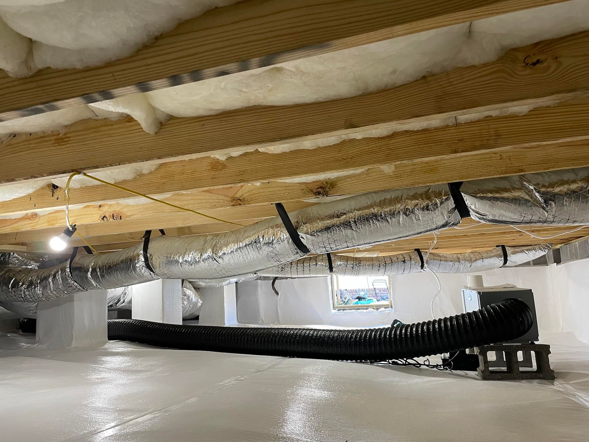 White crawlspace with ducts, insulation, and a black hose.