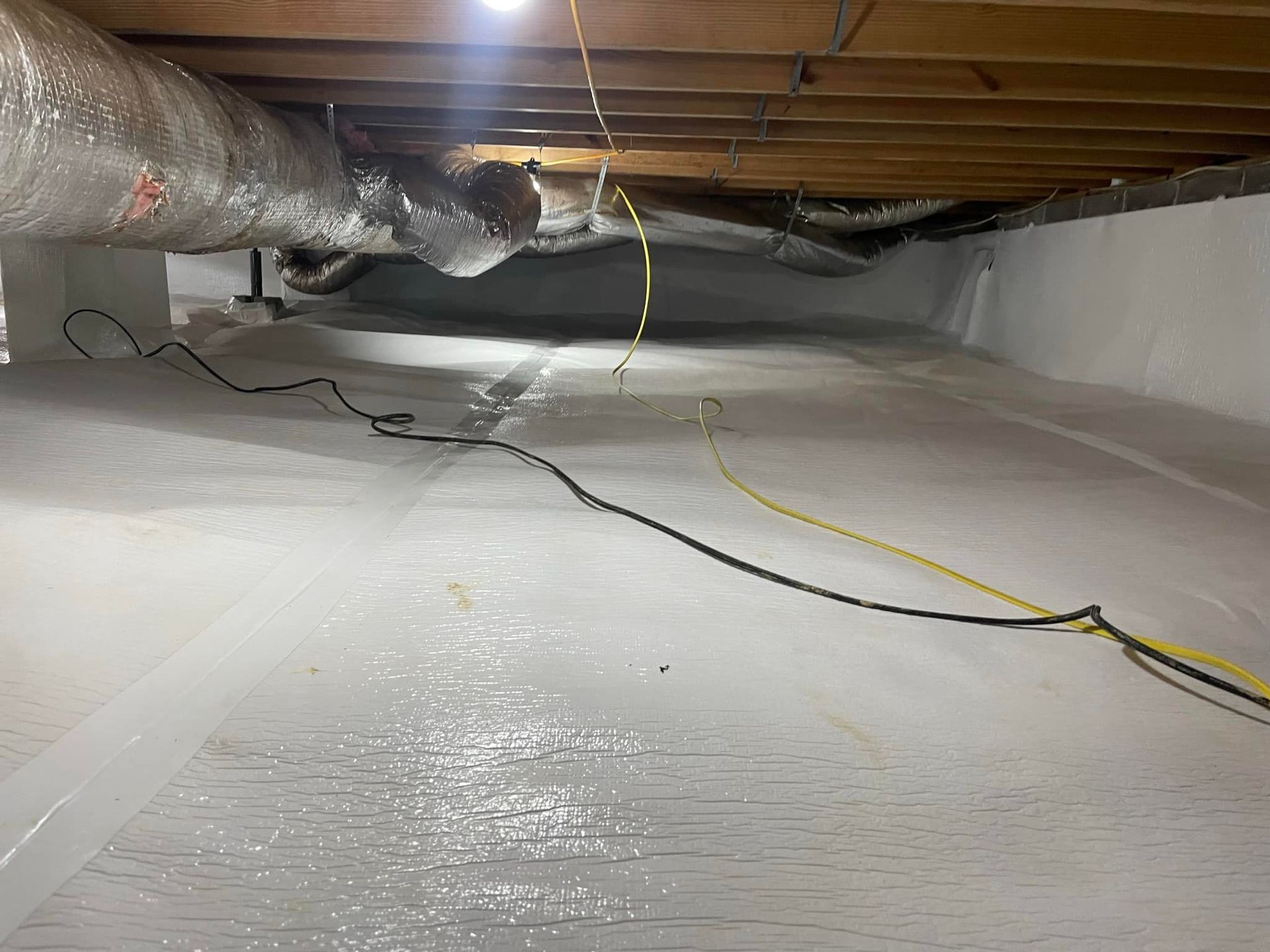 White crawl space with vapor barrier on floor and walls; ductwork and wires visible.
