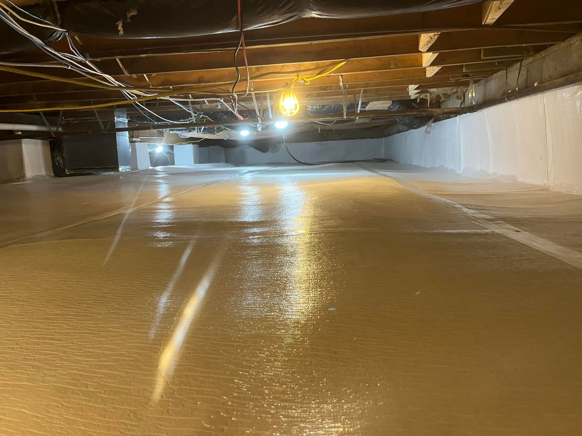 Crawlspace coated in a light gray substance, with white walls and exposed wooden beams above.