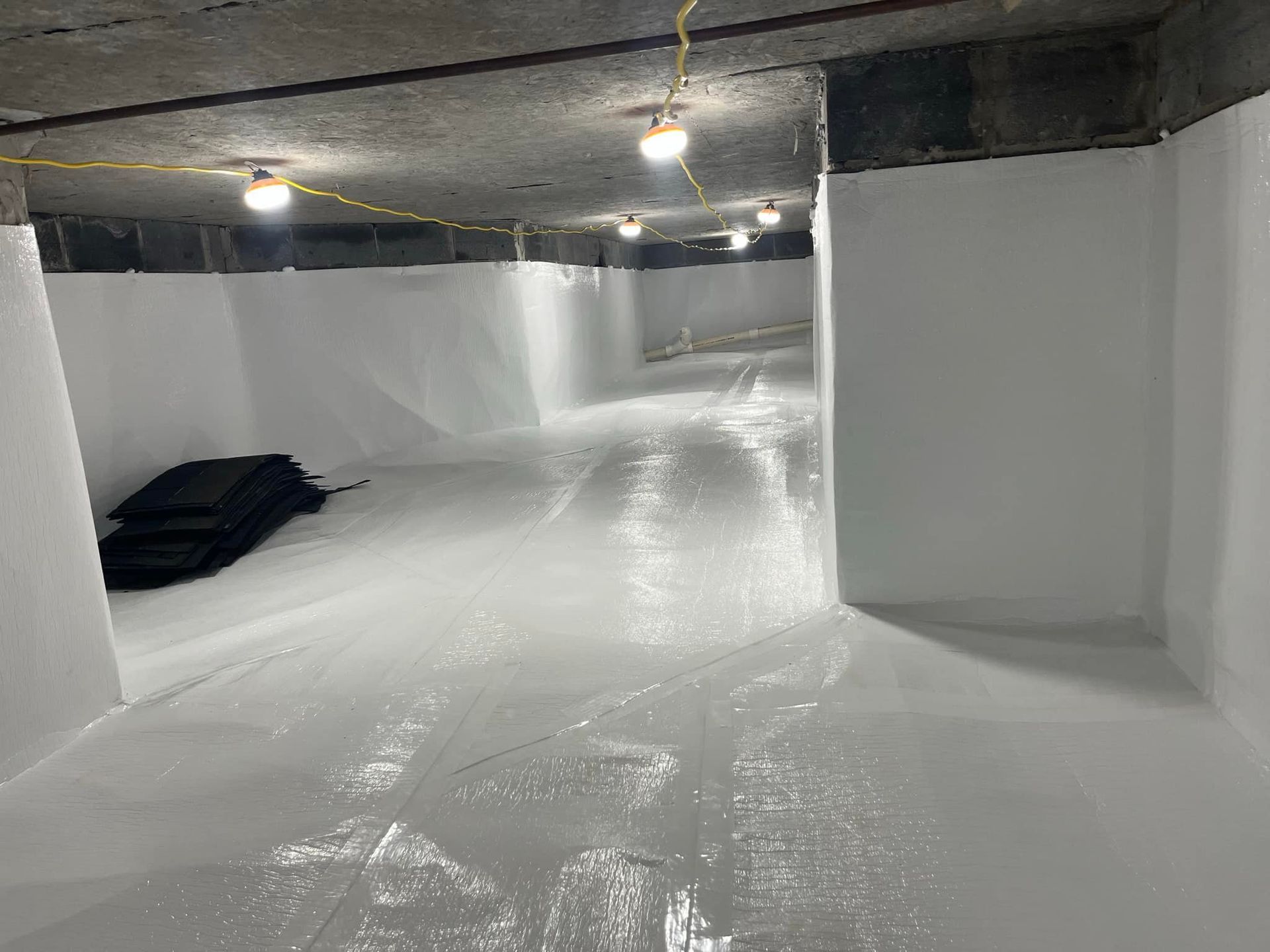 A long, white-walled basement under construction, with overhead lighting and plastic sheeting on the floor.
