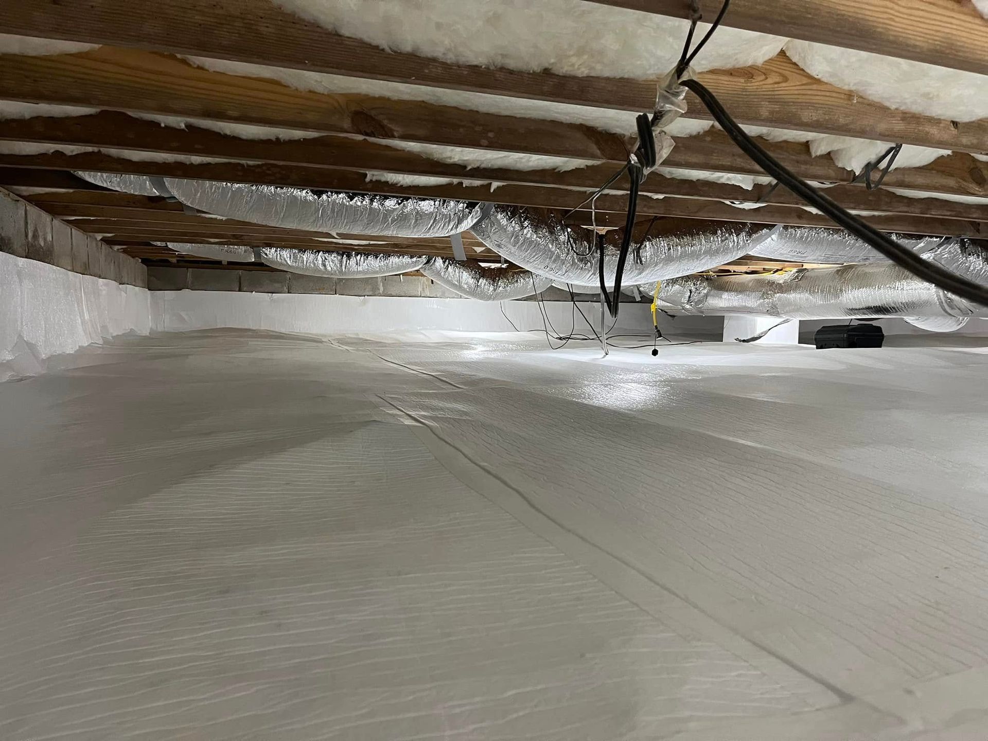 Crawl space with white insulation on walls and floor; ductwork and wiring visible overhead.