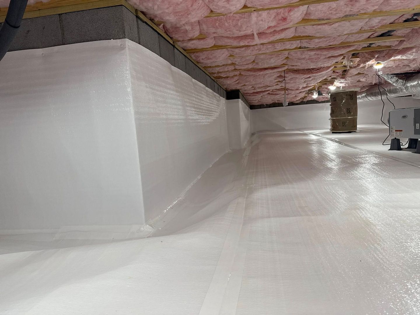 White-walled crawl space with pink insulation, a dehumidifier, and vapor barrier.