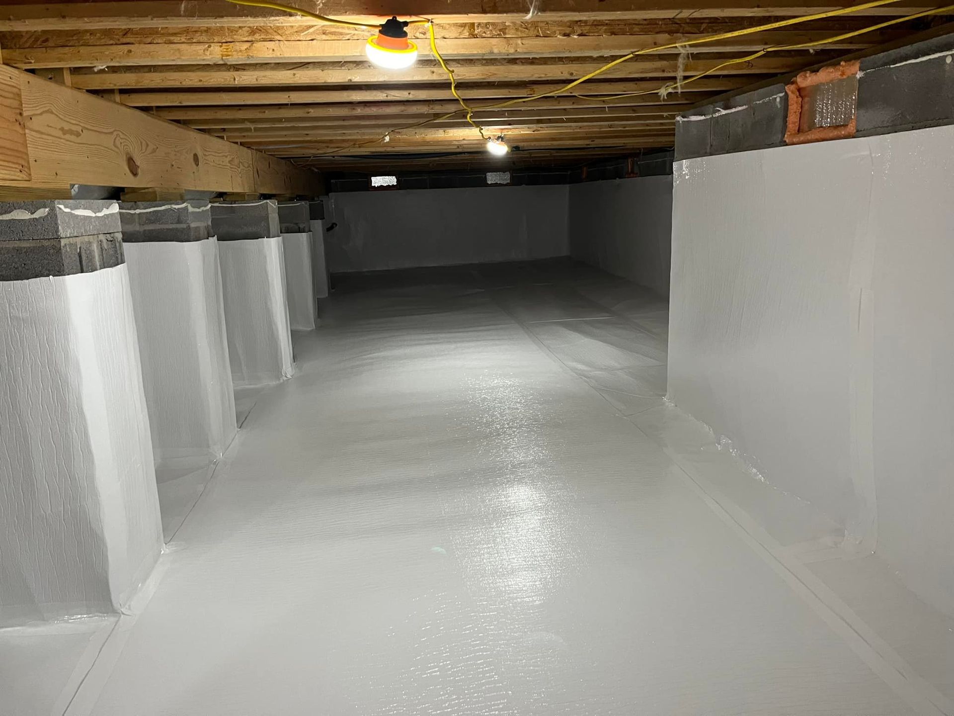 Clean, white crawl space with support posts, wooden beams, and a light-colored floor.