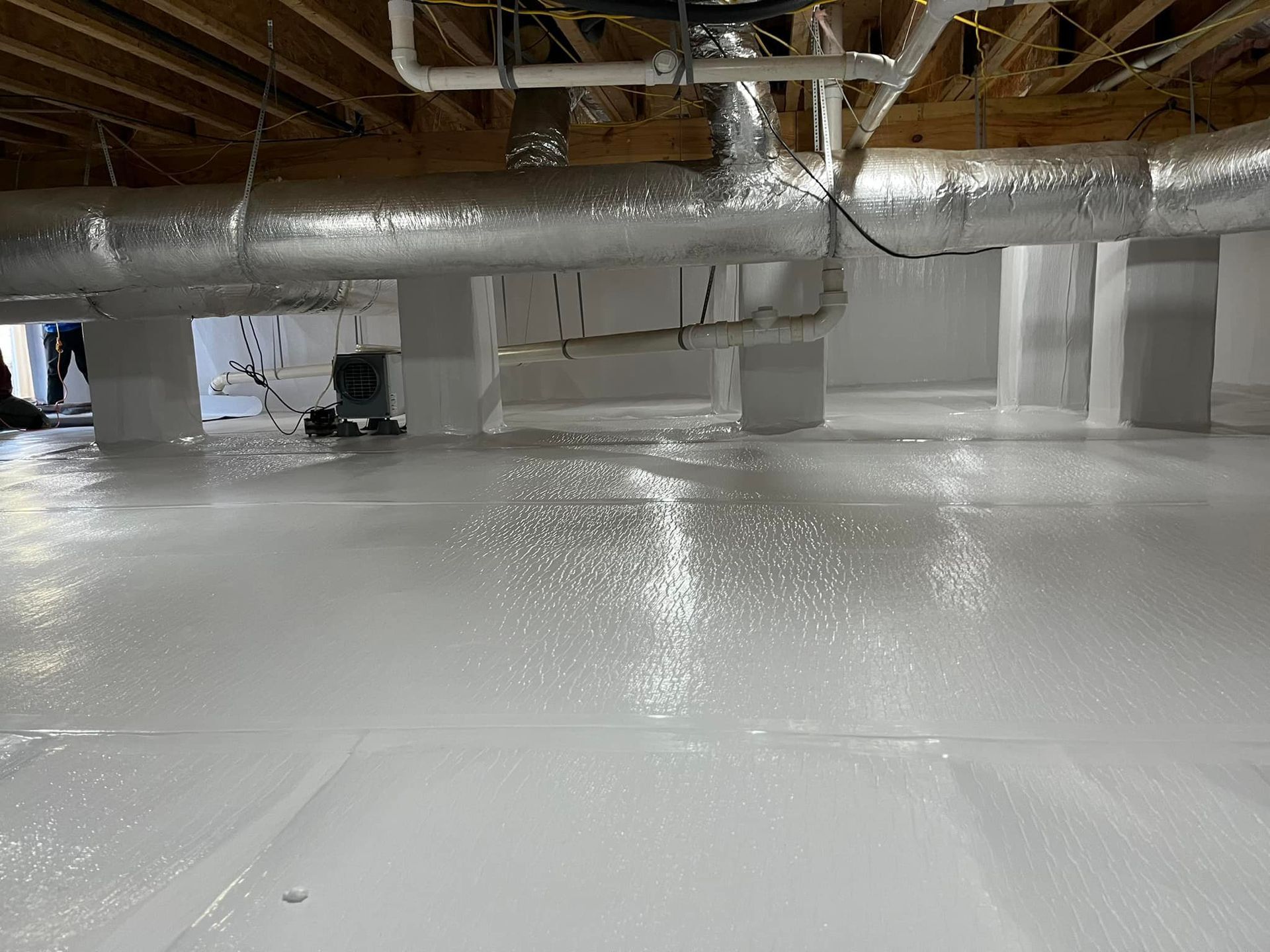 White-painted crawlspace with a reflective floor and exposed pipes and supports.