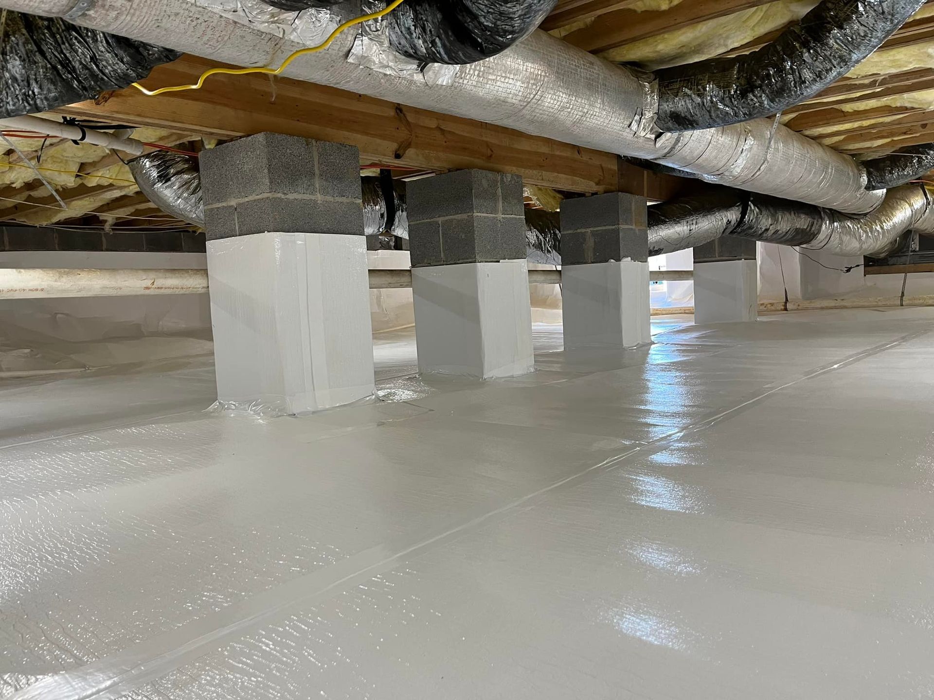 Crawlspace with concrete block supports and a white, reflective floor coating. Ductwork and beams are visible overhead.
