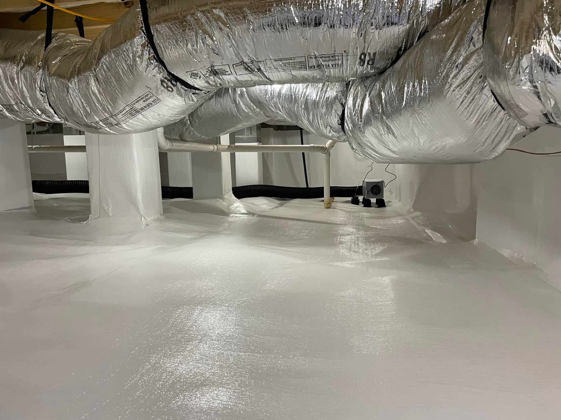 White-walled crawl space with silver ductwork overhead, covered in reflective coating.