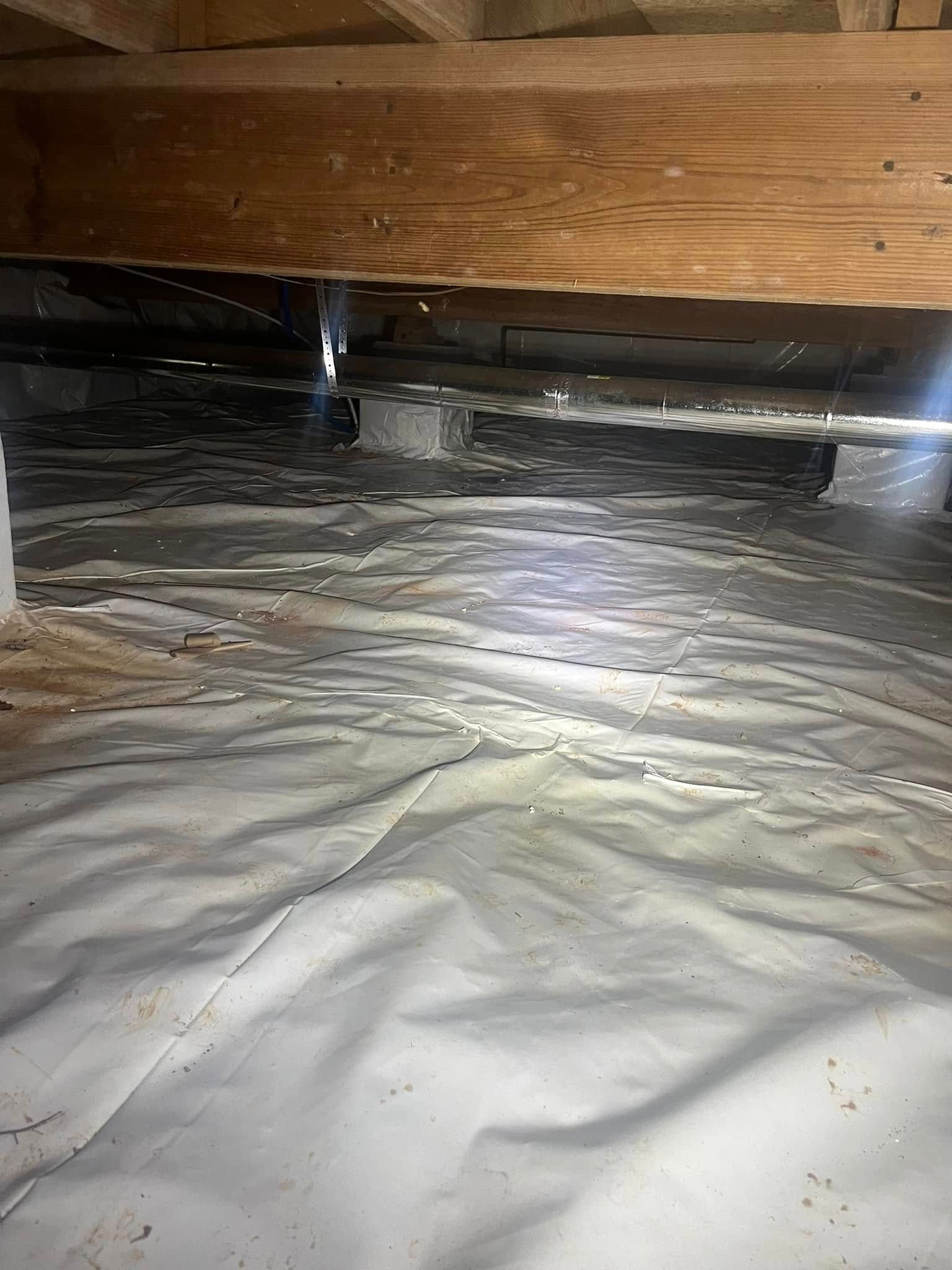 Crawlspace with white vapor barrier, wood beams, and concrete blocks supporting structure.