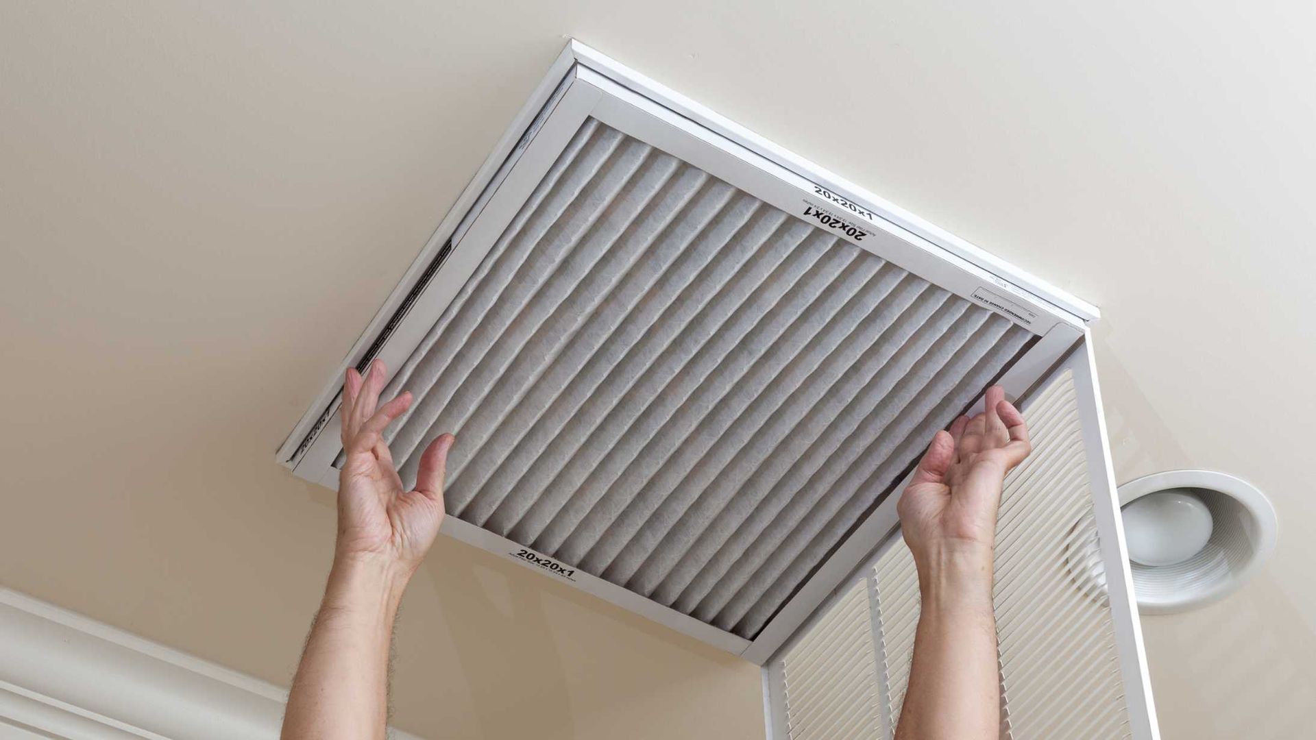 A person is cleaning a ceiling vent with a filter.